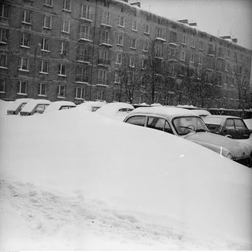 Zaspa śnieżna i zasypane samochody na parkingu. Na pierwszym planie samochód Syrena 