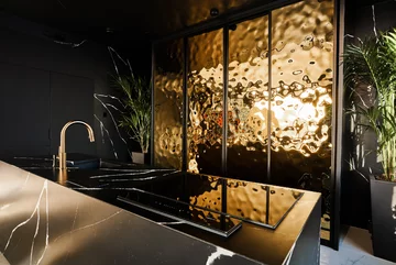 Garderoba kuchenna skryta jest za złotymi drzwiami suwanymi. Intryguje ich ciekawa, nieregularna faktura 