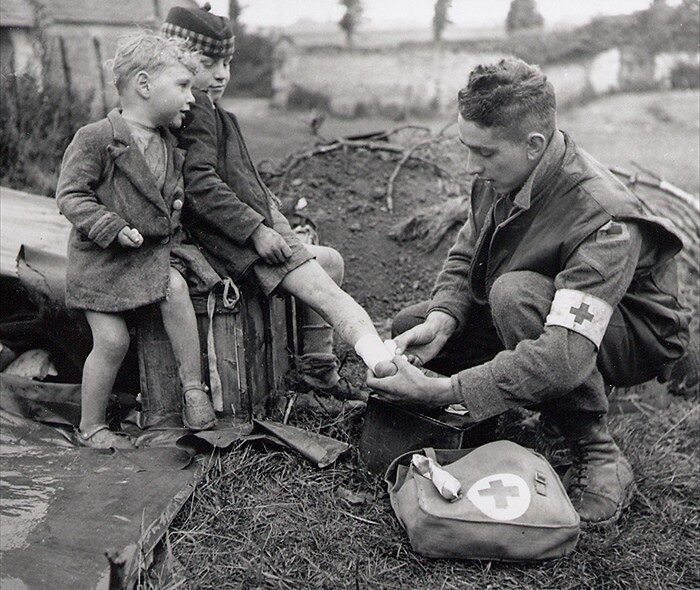 Amerykański lekarz opatruje rannego niemieckiego chłopca, któemu towarzyszy młodszy brat (II Wojna Światowa, 1945)