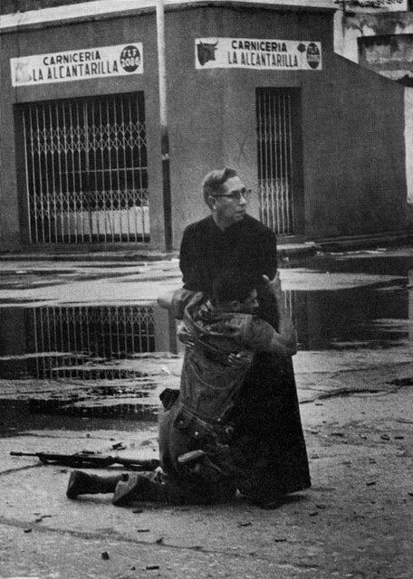 Ranny żołnierz osłaniany przez księdza przed ostrzałem snajperskim (Powstanie El Porte&#241;azo, 1962)