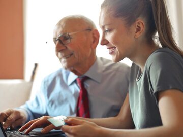 Młoda kobieta pomaga starszemu mężczyźnie w płaceniu kartą kredytową w Internecie za pomocą laptopa