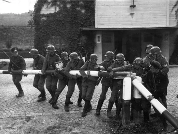 Zdjęcie propagandowe odtwarzające wkroczenie Niemiec do Polski 1 września 1939 r. „Kampania polska pod Gdańskiem. Usunięcie rogatki z polskim herbem na granicy niemiecko-polskiej przez żołnierzy niemieckich” – brzmi propagandowy napis pod zdjęciem