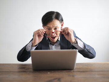 Zdjęcie ilustracyjne, mężczyzna patrzy na laptopa z zaskoczeniem