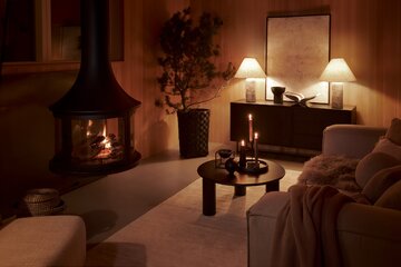 Salon w&nbsp;stylu Comfortcore jest oświetlony nastrojowo przez lampy stołowe, świece i&nbsp;ogień płonący w&nbsp;kominku