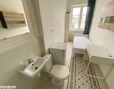 Miniatura: Sedes obok łóżka, lodówka naprzeciwko....