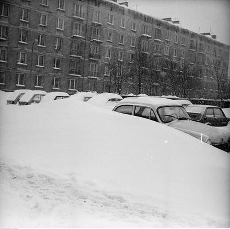 Zaspa śnieżna i zasypane samochody na parkingu. Na pierwszym planie samochód Syrena 