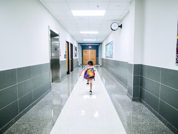 Zdjęcie ilustrucyjne, dziewczynka biegnie wzdłuż szkolnego korytarza