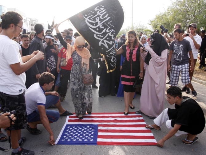 Demonstraci w Tunisie depczą amerykańską flagę i wymachują flagą dżihadystów (fot. PAP/EPA/STR)