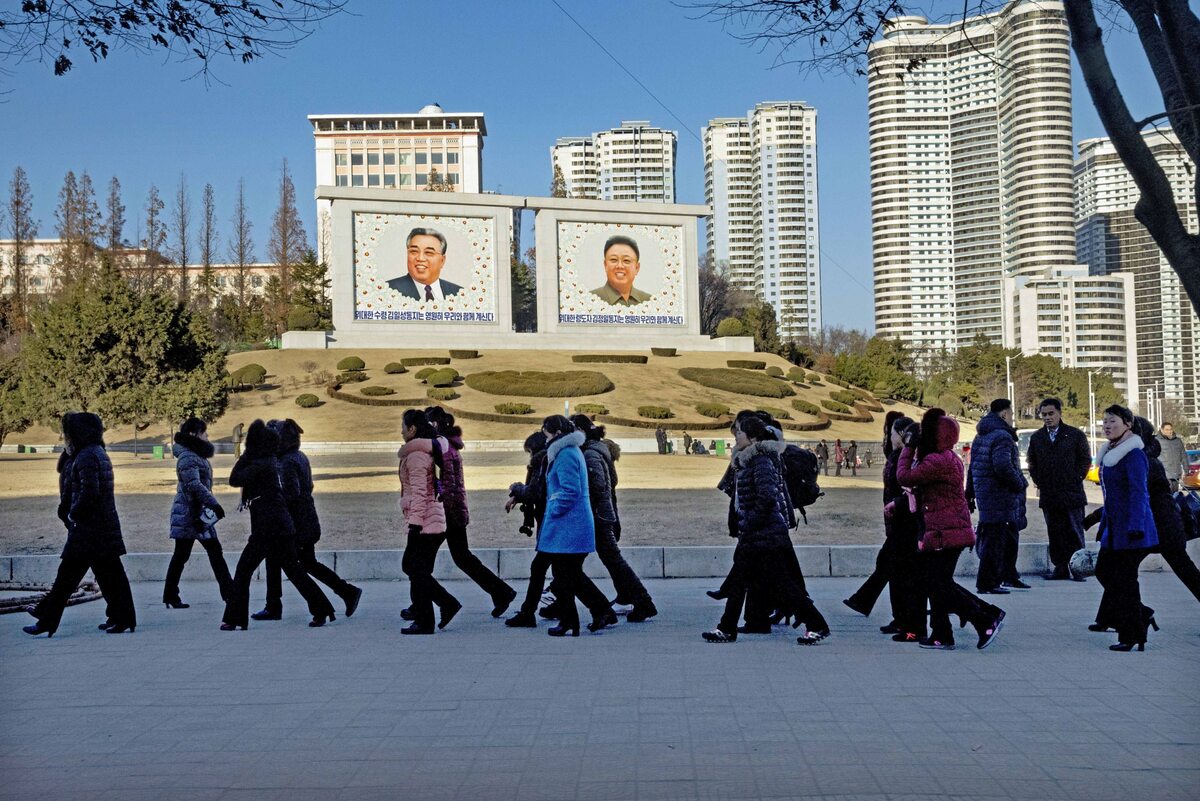 Koreańczycy, w tle podobizny Kim Ir-Sena i Kim Dzong-una 