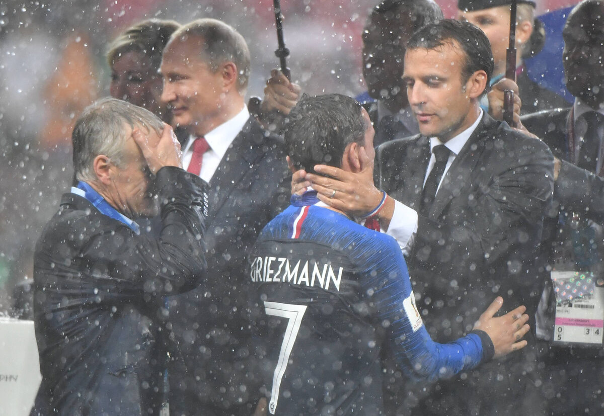 Przemoczony Emmanuel Macron gratuluje Antoine'owi Griezmannowi, obok trener Didier Deschamps 