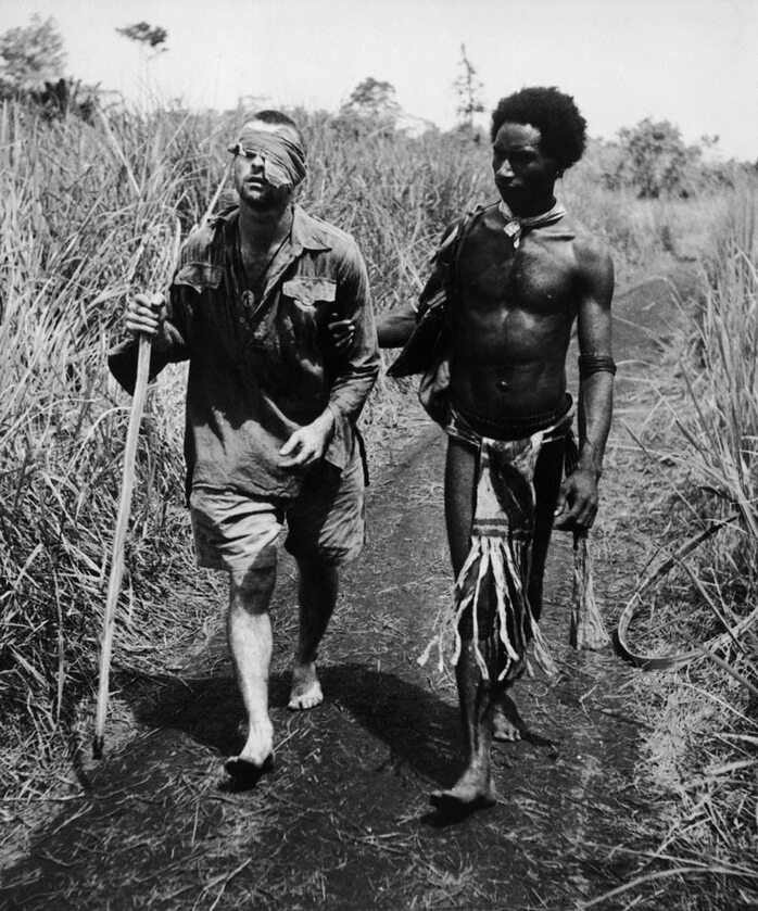 Tubylec z wysp Papui Nowej Gwinei, nazwany przez żołnierzy "Fuzzy Wuzzy Angel" z powodu zmierzwionej fryzury i dobroci, pomaga wyjść z dżungli rannemu australijskiemu żołnierzowi (II WŚ, 1942)