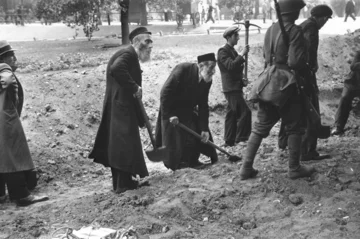 Starsi Żydzi ubrani w charakterystyczne okrycia (chałaty) biorą udział w kopaniu rowów przeciwpancernych, prace nadzoruje wojsko 