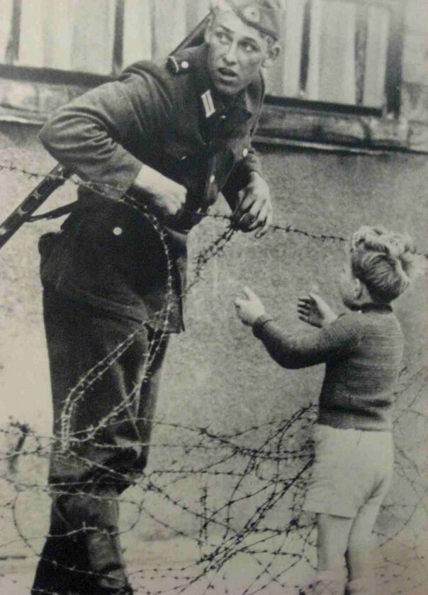 Żołnierz z NRD pomaga przedostać się chłopcu, którego rodzina została w zachodnim Berlinie (1961)