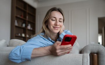 Kobieta korzystająca z&nbsp;smartphona na&nbsp;kanapie w&nbsp;salonie