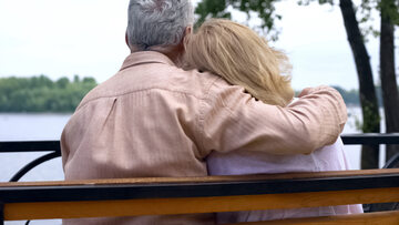 Emerytowany mężczyzna odpoczywa przytulając żonę na ławce w parku w pobliżu rzeki, zdjęcie ilustracyjne