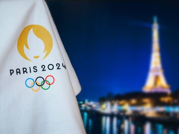 Flaga igrzysk olimpijskich w Paryżu, a w tle Wieża Eiffla