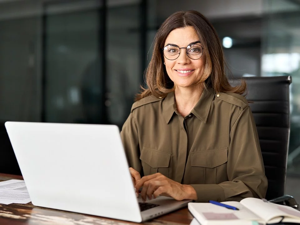 Uśmiechnięta kobieta w biurze, pracująca na laptopie