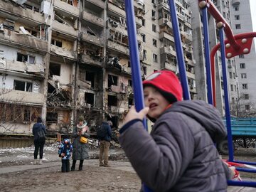 Kijów. Dziecko na huśtawce przy zniszczonym bloku w stolicy Ukrainy, 26 lutego