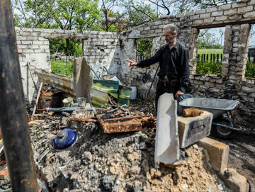 Mieszkaniec wsi Bohorodychne w obwodzie donieckim pokazuje zniszczony dom, 26.05.2023 r.