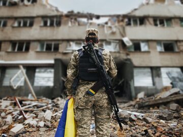 Obrończyni Ukrainy z ukraińską flagą w rękach na tle eksplodującego domu