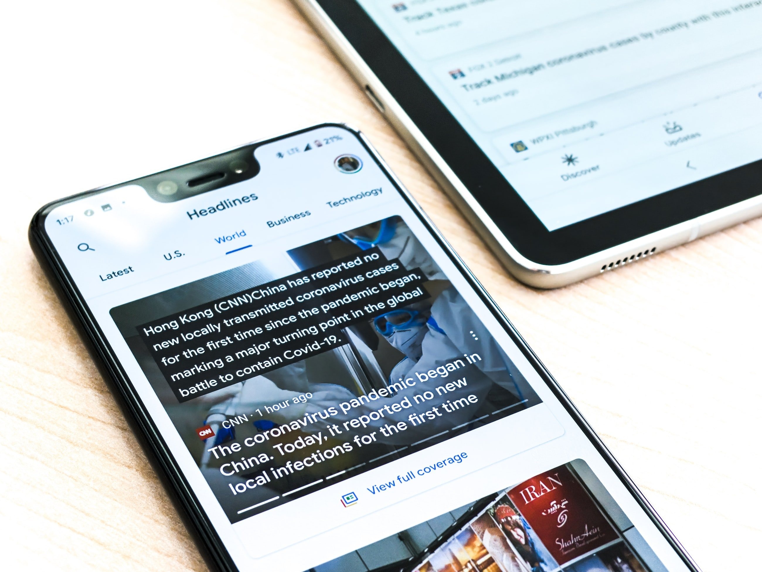 A Google pixel 3XL showing Covid-19 information from the Google News app sits on a wooden table next to a Samsung Galaxy Tablet