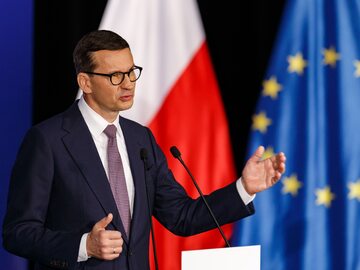 Premier Mateusz Morawiecki na tle flag: polskiej i unijnej