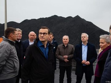 Premier Morawiecki w otoczeniu współpracowników na tle importowanego węgla