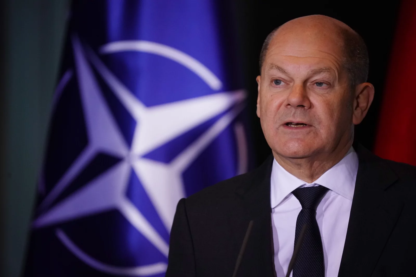 Olaf Scholz na tle flagi NATO