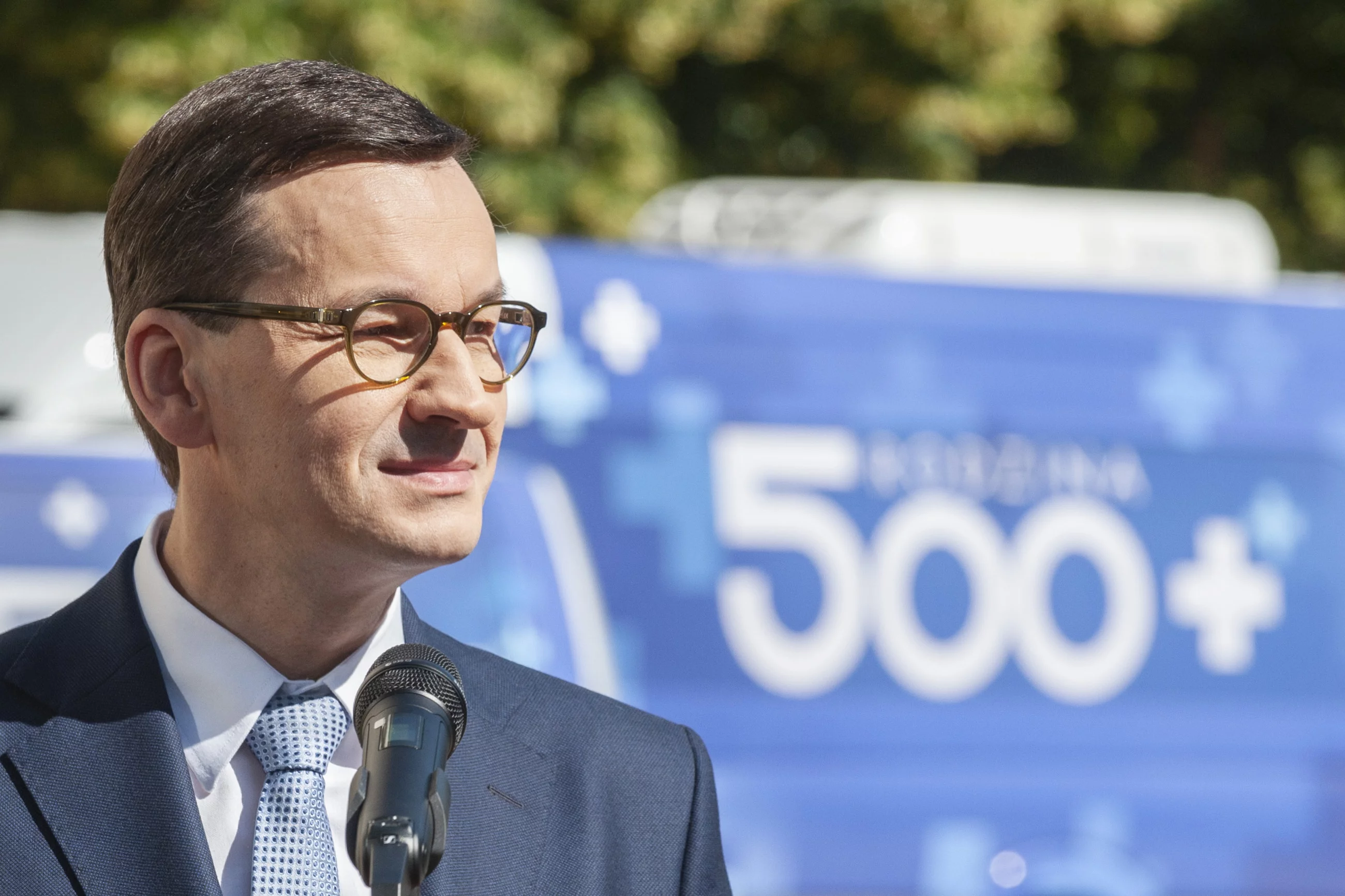 Mateusz Morawiecki na tle busa z logiem programu 500 plus