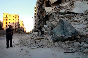 Starszy mężczyzna patrzy na ruiny budynku w Aleppo