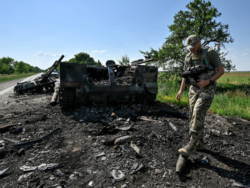 Ukraiński żołnierz obok zniszczonego rosyjskiego pojazdu