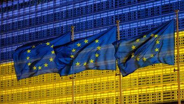 Unijne flagi na tle podświetlonej w barwach Ukrainy siedziby Komisji Europejskiej w Brukseli.