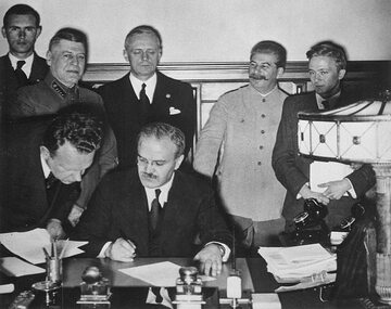 Wiaczesław Mołotow podpisuje radziecko-niemiecki Pakt o Nieagresji, 23 sierpnia 1939 roku. Z tyłu stoi Joachim von Ribbentrop i uśmiechnięty Józef Stalin