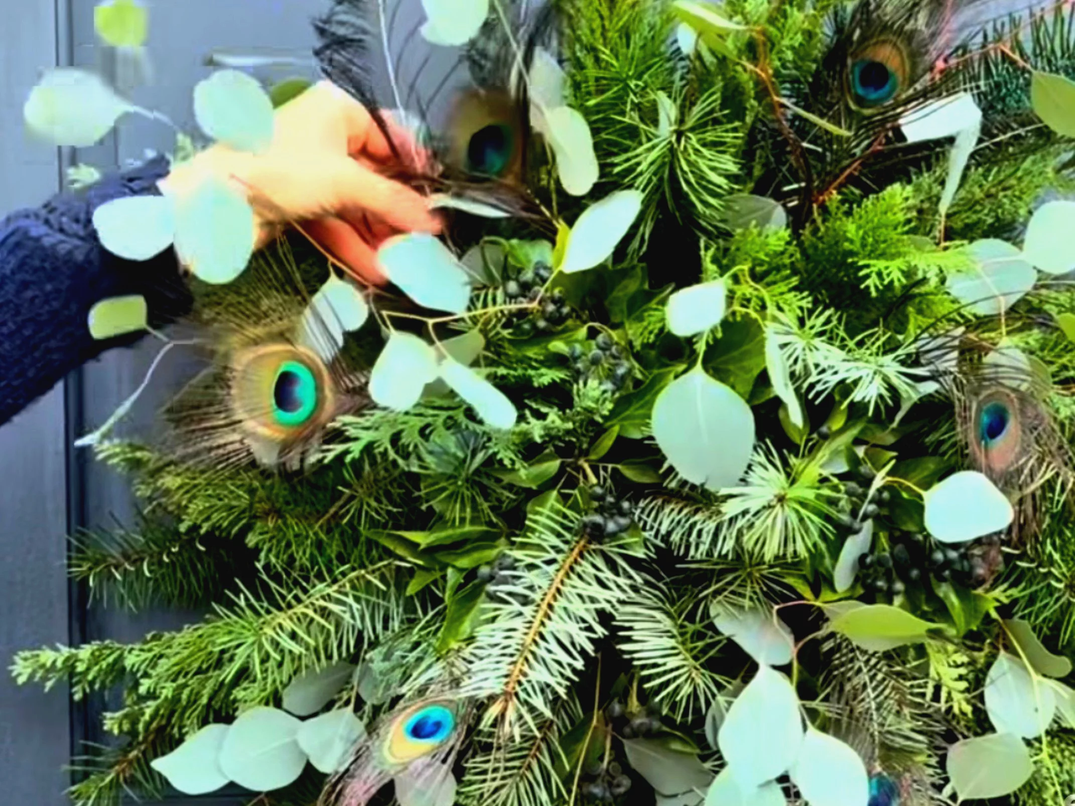 Naturalny wianek na drzwi wykonany z ziemniaka, świeżych gałązek jodły, bukszpanu i cyprysa, ozdobiony pawimi piórami oraz granatową wstążką – ekologiczna dekoracja DIY inspirowana naturą